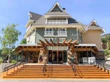 The Chimney Rock Grill entrance in the Selkirk Lodge at Schweitzer village, with wide wooden steps leading up to its stone and timber entryway.