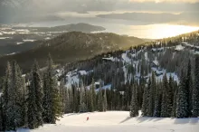 A skier descends a snowy Schweitzer slope above the village, with Lake Pend Oreille glowing in the distance.