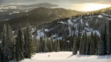 A lone skier on a snowy Schweitzer slope above the village and Lake Pend Oreille at sunset.