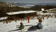 Vintage photograph of skiers outside Schweitzer's early day lodge, with snow-covered slopes and Lake Pend Oreille in the distance