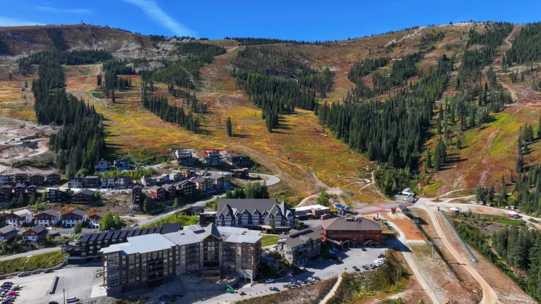 Schweitzer village in fall below the ski slopes under a clear blue sky, with autumn color on the mountain.