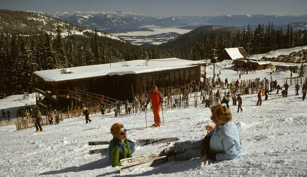 Vintage photograph of skiers outside Schweitzer's early day lodge, with snow-covered slopes and Lake Pend Oreille in the distance